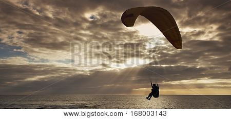 Silhouette of flying paraglider over the sea sunset