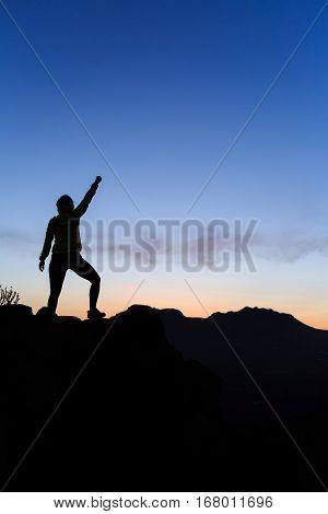 Woman hiking silhouette in mountains sunset and ocean. Female hiker climber or trail runner with arms outstretched on mountain top looking at beautiful night sunset inspirational landscape.