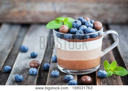 Delicious three layered chocolate mousse dessert decorated with fresh blueberry mint and candies served in glass cup