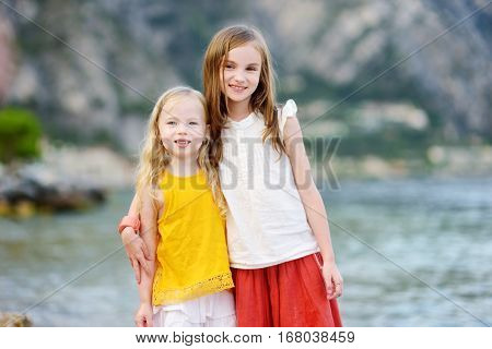 Two Cute Little Sisters Having Fun On A Beach Of Limone Sul Garda, A Small Town And Comune In The Pr