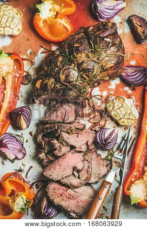 Cooked Roastbeef meat with roasted vegetables and herbs in metal baking tray, top view, vertical composition. Slow food concept