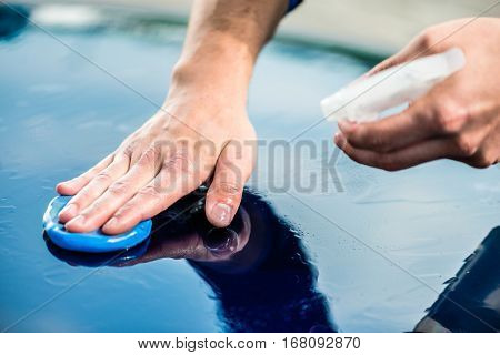 Close-up of male hands waxing the surface of a blue car at auto wash