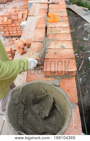 Bricklaying. Bricklayer worker installing red brick wall with trowel putty knife outdoor. Basic Bricklaying.