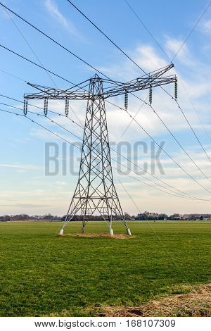 Power pylon and high voltage lines in an agricultural landscape in the Netherlands. In the background is the edge of a small village. It is a sunny day in the winter season.