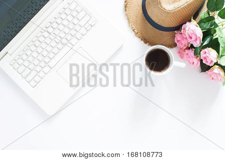 Flat lay of computer laptop with casual hat a cup of coffee and pink roses Top view on white background with copy space
