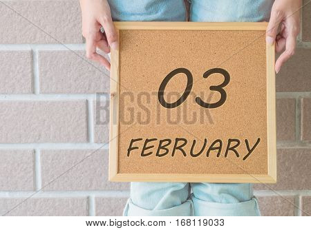 Closeup calendar at the cork board in hand of asian woman in front of her legs with 3 february word on brick wall textured background