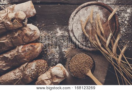 Bread background. Brown and white whole grain loaves wrapped in kraft paper composition on rustic dark wood with empty desk copy space. Baking and home bread making concept. Soft toning