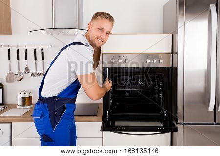 Young Male Technician Repairing Oven In Kitchen