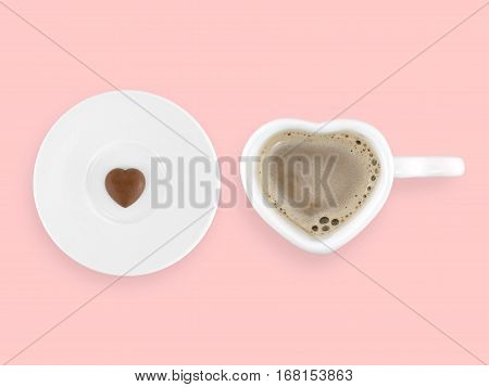 coffee in heart shape cup and tiny heart shape chocolate on white ceramic saucer isolated on pastel pink background, sweet confectionery and beverage for Valentine\'s Day, flat lay close-up top view