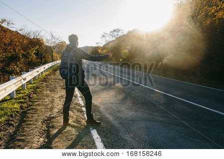 Man hitchhiking on a country road. Traveler showing thumb up on for hitchhiking during road trip. Adventure and tourism concept.