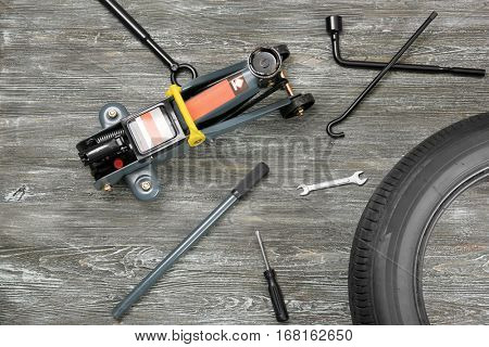 Car jack with tools and tire on wooden background