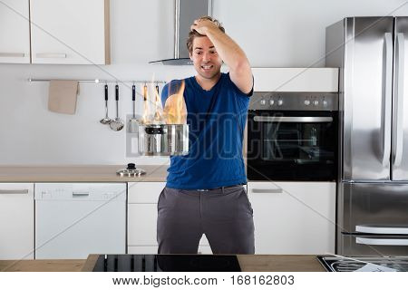 Young Surprised Man Holding Utensil On Fire In Kitchen