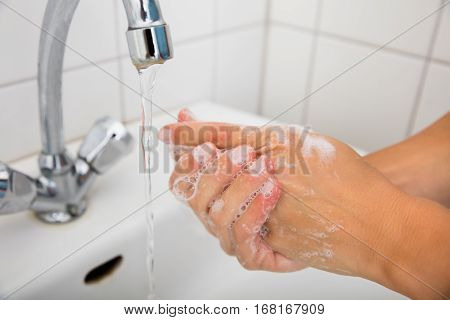 Close-up Of Woman Applying Soap While Washing Hands In Basin With Open Tap