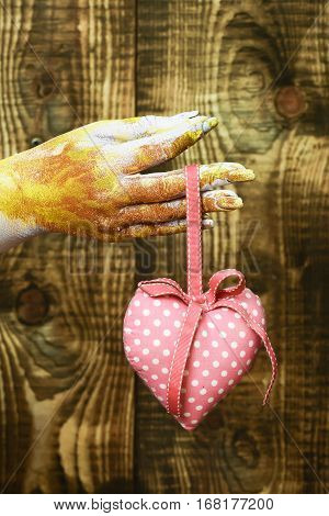 female hand smeared in golden paint or glister holding handmade pink polka dots valentine heart on brown vintage studio background selective focus
