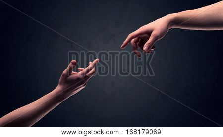 Two male hands reaching out to one another, almost touching, in front of dark clear empty background wall concept
