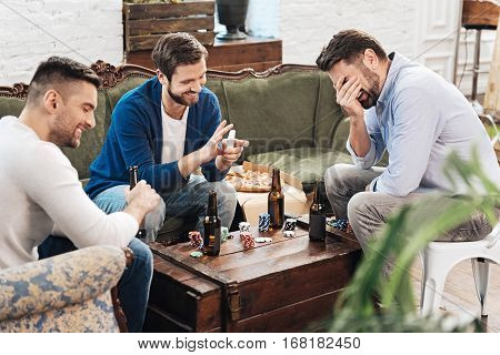 Playing card games. Happy joyful positive man holding a pack of cards and laughing while playing card games with his friends