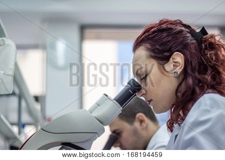 Female and male medical or scientific researchers or women and men doctors looking through a microscope in a laboratory. Young scientist doing some research.