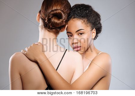 I have got your back. Two amazing committed professional models working on a photoshoot in a studio while one of them turning back on the camera and the other hugging her partner by her shoulder