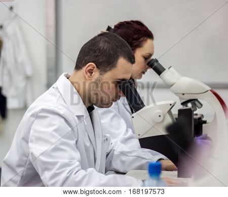 Female And Male Medical Or Scientific Researchers Or Women And Men Doctors Looking Through A Microsc