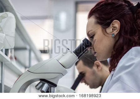 Female And Male Medical Or Scientific Researchers Or Women And Men Doctors Looking Through A Microsc