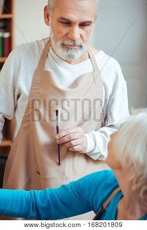 Pleasant time. Concentrated professional artist giving advice to his female colleague while working together and painting.