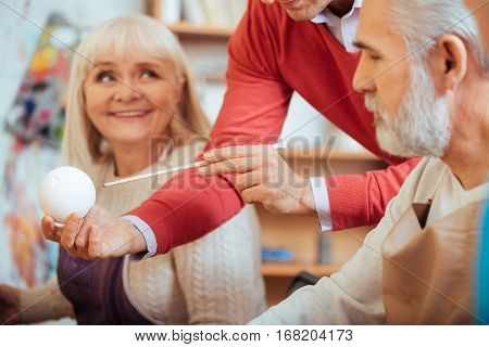 Attentive listeners. Close up of professional artists hands demonstrating a ball while man and woman listening to him and spending time in painting school.