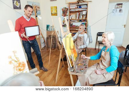 Have it. Handsome young talented man demonstrating a painters diploma while standing in painting school and spending time with his colleagues.