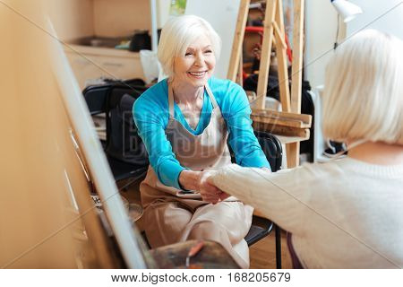 Creative cooperation. Elderly happy ambitious women talking and laughing in painting class while drawing.