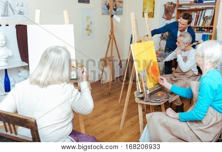 Find yourself. Group of concentrated elderly delighted people having lesson while spending time in painting school and listening to lecturer.