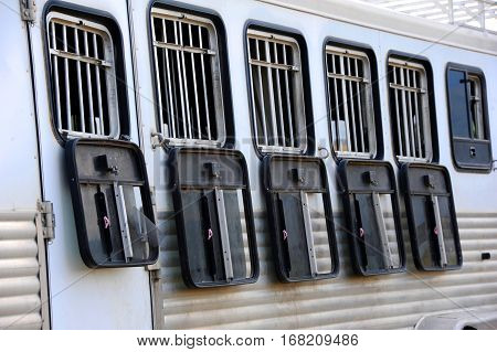 Aluminum horse trailor is silver and has open windows. Black molded plastic window covers hang below windows.