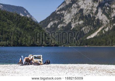 Couple reading book and newspaper on lake Leopoldsteiner near Eisenerz in Styria Austria