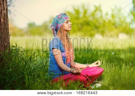 Young girl meditating in the park. Girl with pigtails in a turban meditating sitting on the grass on a sunny day