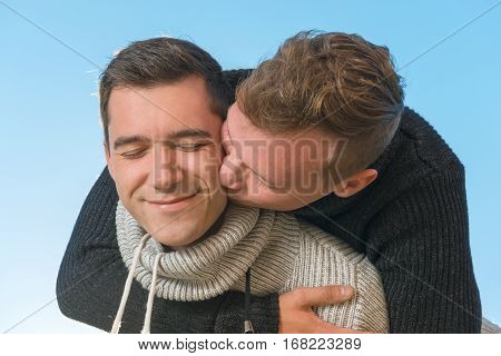 Gay couple hugs and kisses his boyfriend outdoors on a background of sky