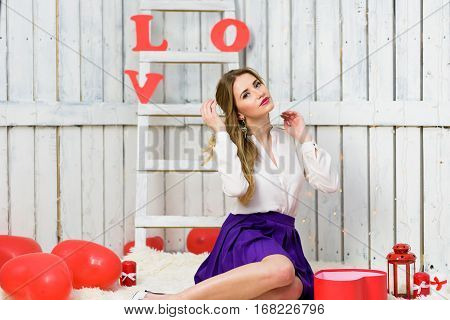 Blonde girl with blue eyes portrait. Romantic scene. Red hearts and lights. Red and White background