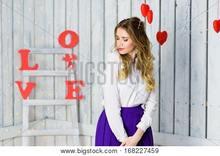 Blonde girl with blue eyes portrait. Romantic scene. Red hearts and lights. Red and White background