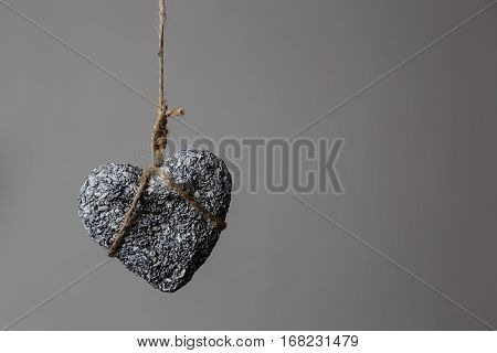 Stone heart in jute bondage hangs against grey background with copy space Valentine's day concept horizontal view