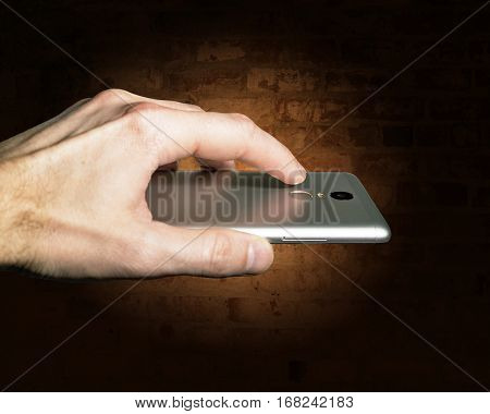 Finger touches the fingerprint scanner on the smartphone against a brick wall