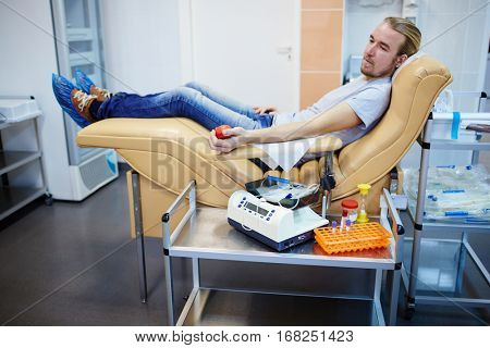 Young man sitting in armchair at hemotransfusion station