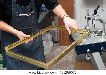 Craftsman working on frame in frameshop. Professional framer hand holding frame angle. Top view.