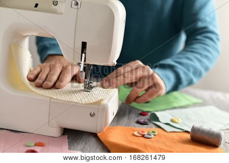 closeup of a young caucasian man sewing a beige fabric with a sewing machine