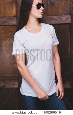 Young woman wearing blank white t-shirt with area for your logo or design, mock-up of template white t-shirt, wooden wall in the background
