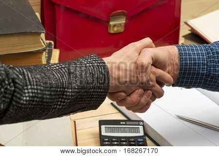 Business concept. Business partners handshaking after signing contract. Pertnership. On a wooden table books documents calculator red briefcase