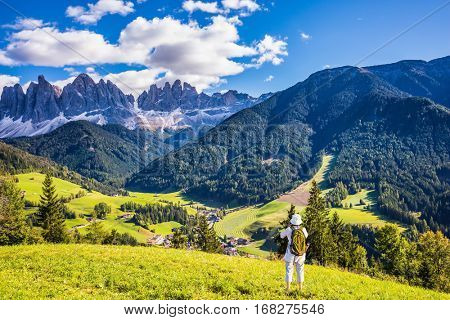 Elderly woman with backpack photographs at Dolomites, Northern Italy. Forested mountains surrounded by green Alpine meadows. The concept of active and eco-tourism