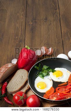 Delicious homemade omelette in vintage frypan with tomatoes, greens, bread and bell pepper on old rustic wooden background, top view. Healthy breakfast with fried egg on skillet pan. copy space