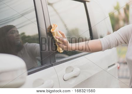 Asian woman washing car window with microfiber cloth