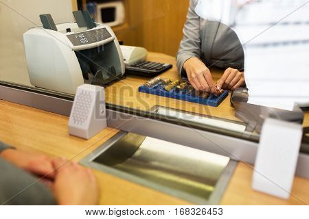 people, money, saving and finance concept - clerk counting coins for customer at bank office or currency exchanger