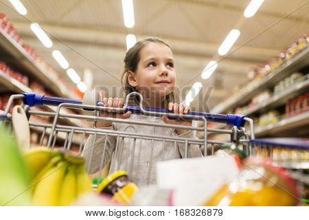 sale, consumerism and people concept - happy little girl with food in shopping cart at grocery store
