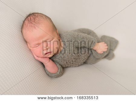 Cute baby in a grey outfit napping with his hand holding his cheek, closeup