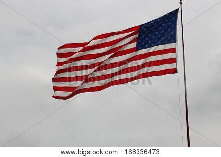 American flag blowing in wind against light gray sky