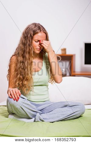 Young woman is sitting in her bed and having pain in sinus.